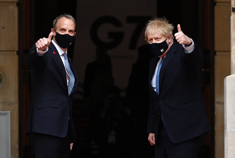 Dominic Raab and Boris Johnson, both wearing face masks, turn and give thumbs up signs to the camera as they enter the G7 conference.