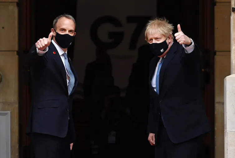 Dominic Raab and Boris Johnson, both wearing face masks, turn and give thumbs up signs to the camera as they enter the G7 conference.