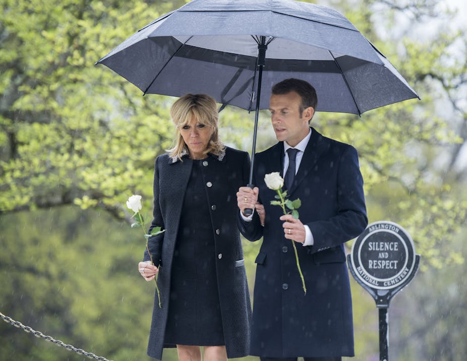 Emmanuel et Brigite Macron marchent main dans la main sous un parapluie.