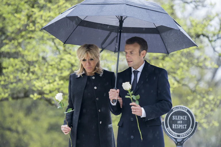 Emmanuel et Brigite Macron marchent main dans la main sous un parapluie.