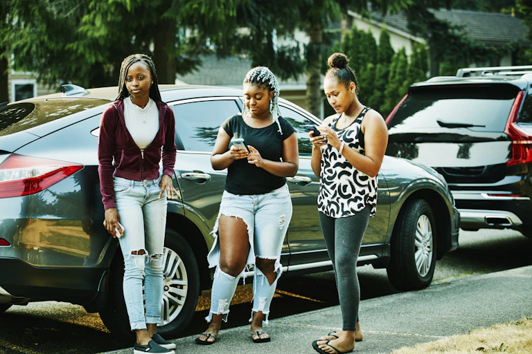 Three teenage girls on a sidewalk looking at smartphones
