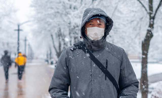 A man outside in winter, wearing a coat and a face mask