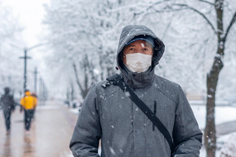 A man outside in winter, wearing a coat and a face mask