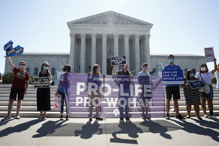 A group of people holding signs in front of the Supreme Court building