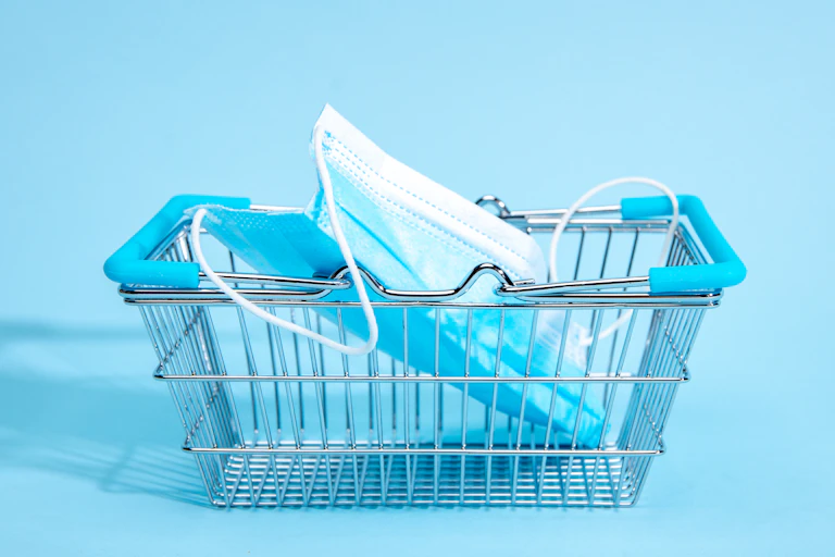 A small shopping cart with a mask in it with a blue background