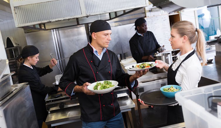 A chef handing a food order to a server in a restaurant kitchen.
