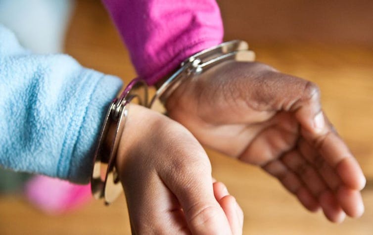 A pair of Black hands are locked together in handcuffs.