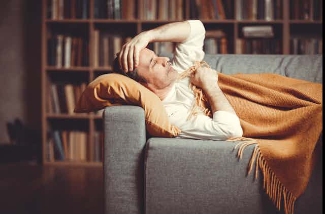 Un homme couché sur un sofa, enveloppé dans une couverture