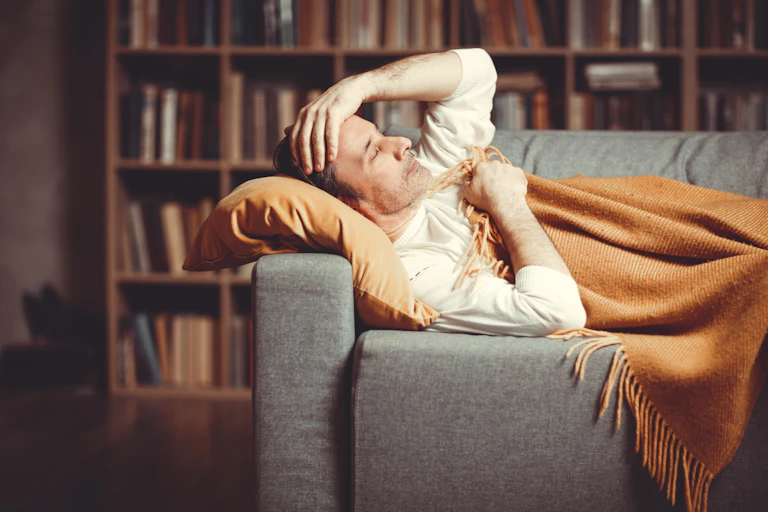 Un homme couché sur un sofa, enveloppé dans une couverture