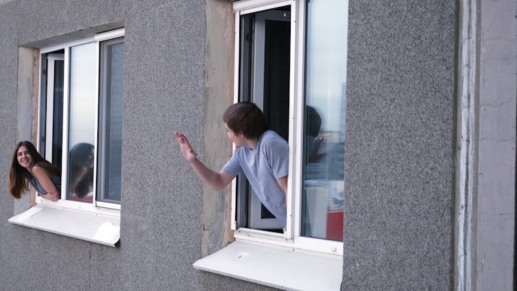Neighbours in adjacent apartment wave to each other.