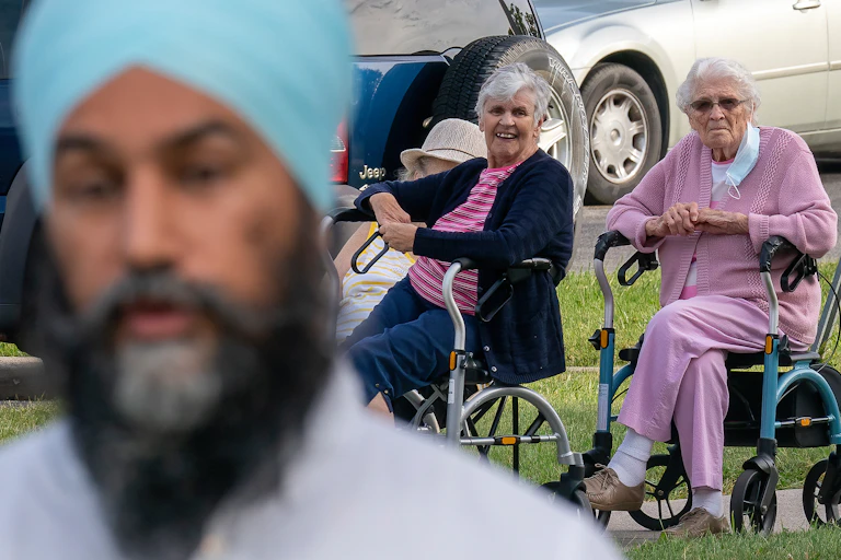 Two women in walkers watch Jagmeet Singh speak