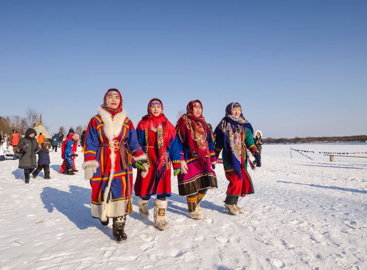 Four young women wearing brightly coloured traditional dress walk over snow.
