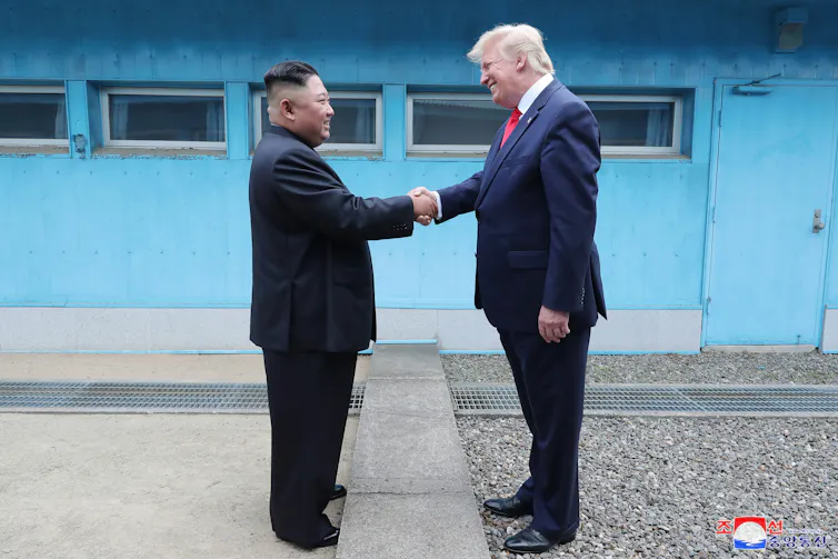 Donald Trump and Kim Jong-un shake hands and smile.