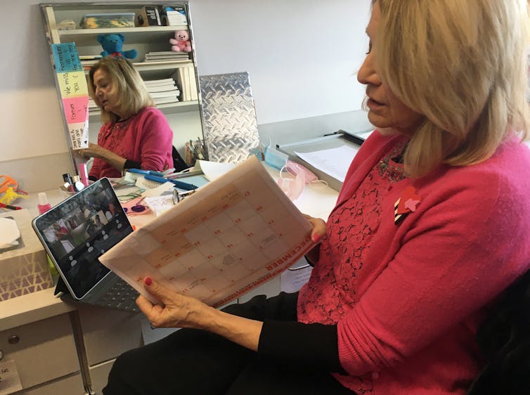 A teacher holds up a calendar to her laptop screen during a Zoom call with her class.