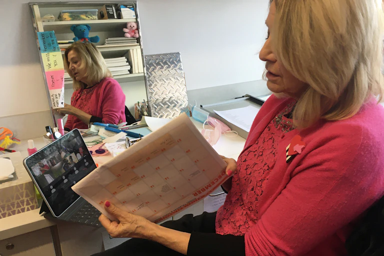A teacher holds up a calendar to her laptop screen during a Zoom call with her class.