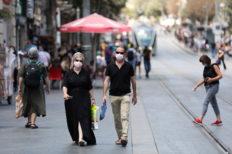 People in masks walking down a street in Israel