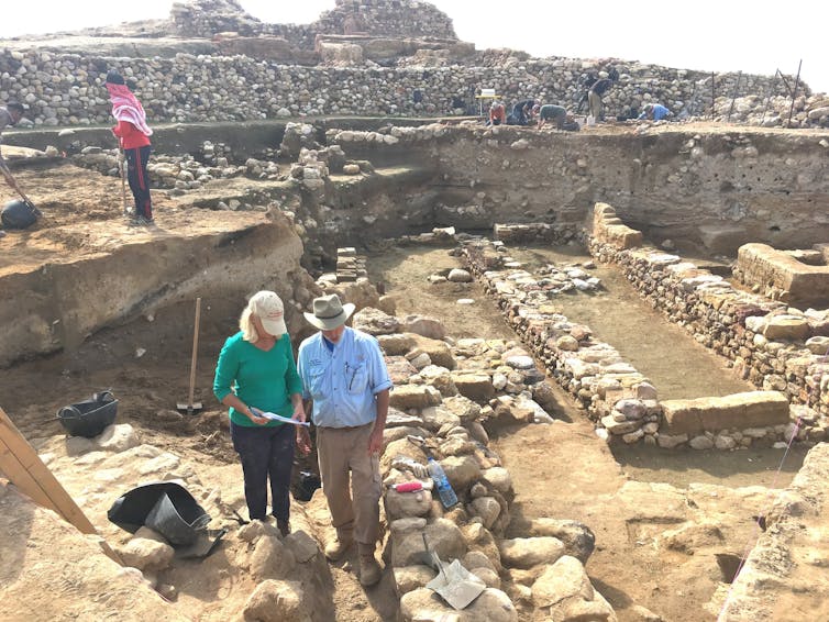 Archaeologists stand in midst of many short stone walls - the ruins of a city.