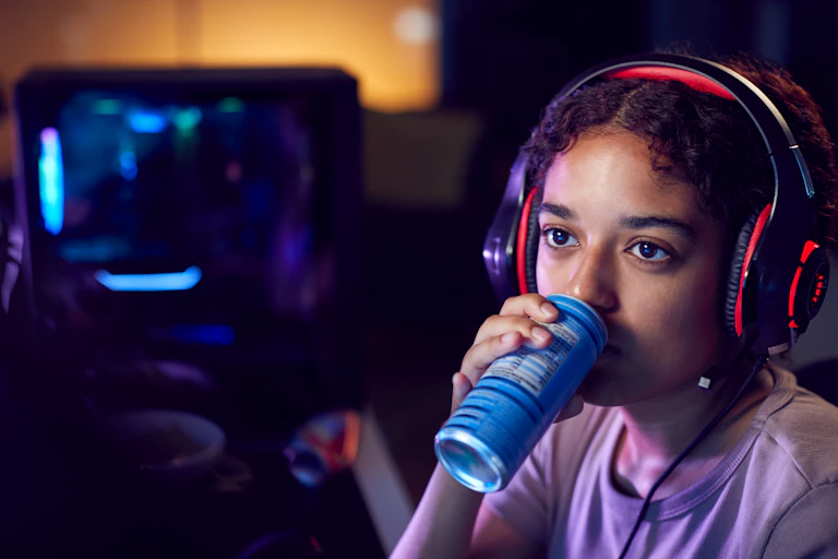 teen girl consumes an energy drink while playing video games
