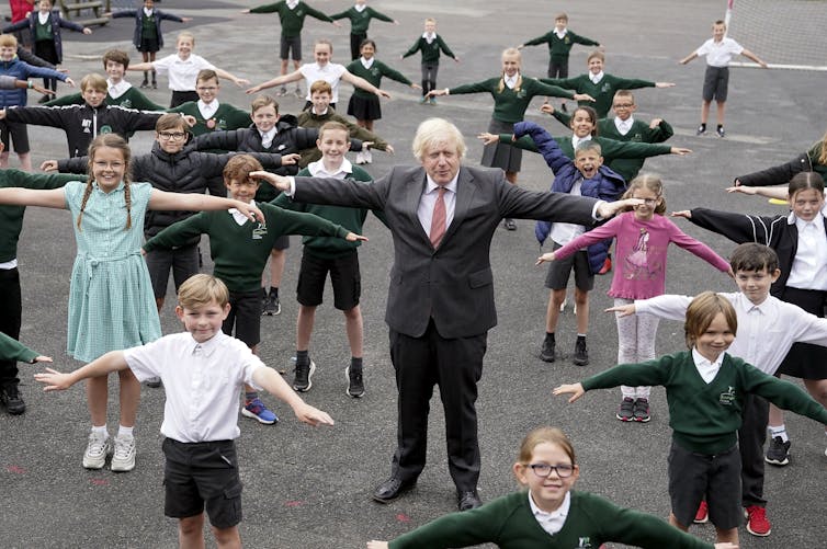 Man in suit stands among children with outstretched arms as they demonstrate physical distancing