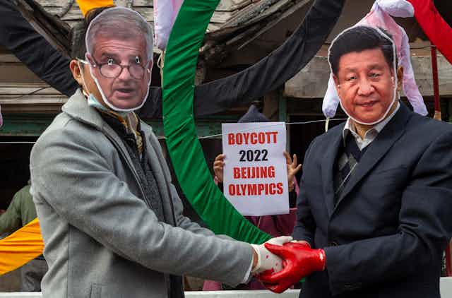 Protesters in masks shake hands while someone holds up a sign that says Boycott 2022 Beijing Olympics