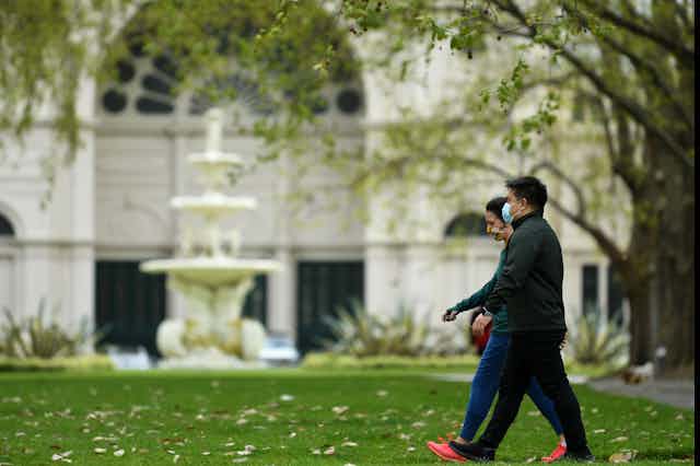 Two people in masks walk outside in a Melbourne park.
