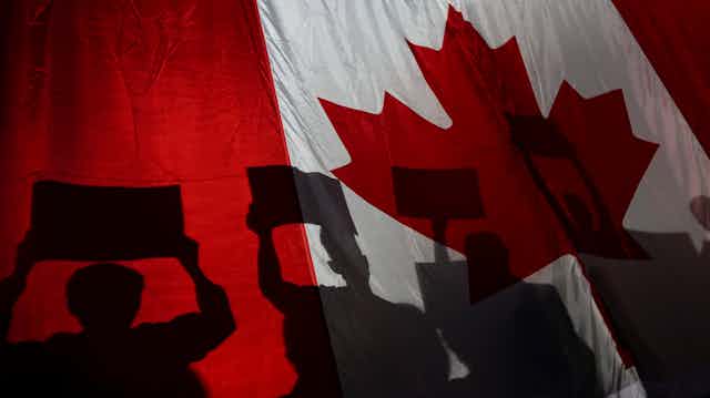 People holding signs are silhouettted in the Canadian flag.