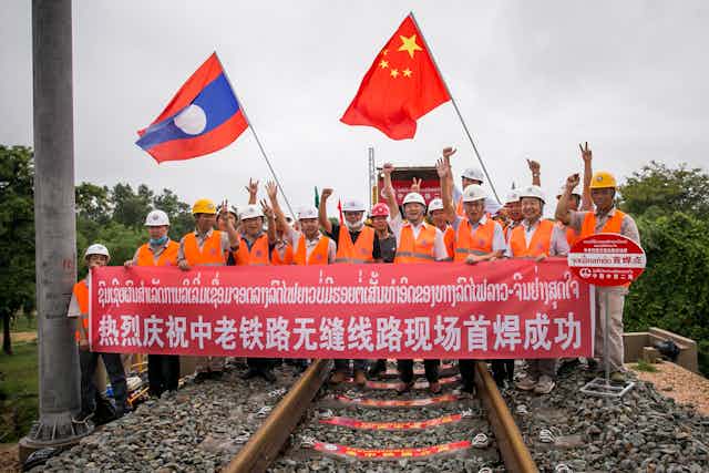 Workers stand on tracks holding banner in Chinese and Laotian.