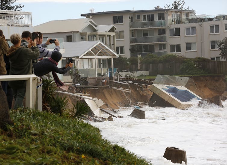 Tourists photograph beachside homes damaged by storm