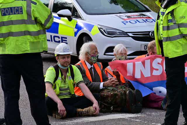 Protesters sit on tarmac surrounded by police.