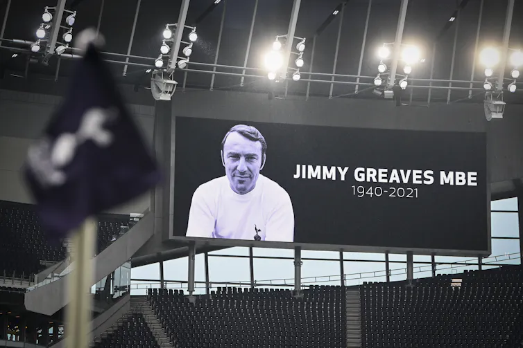 A video screen above a football stand displays a tribute to Jimmy Greaves.