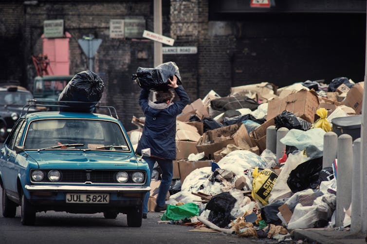 A boy surrounded by rubbish as a car drives past