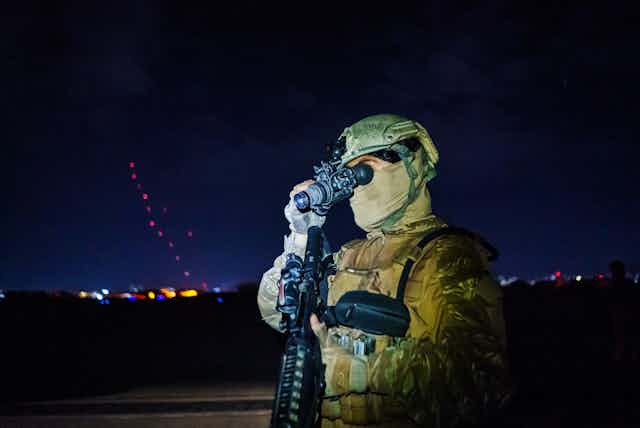 A person in camouflage clothing looks through a night vision device
