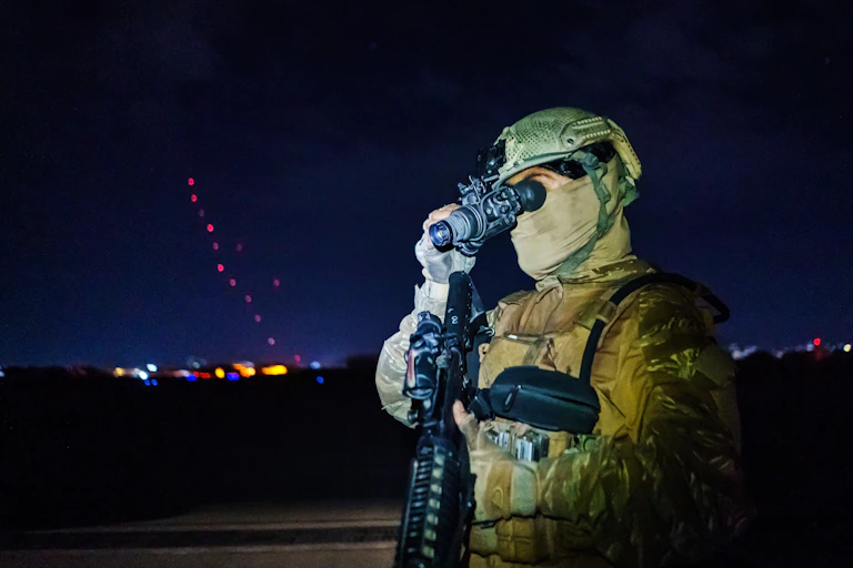 A person in camouflage clothing looks through a night vision device