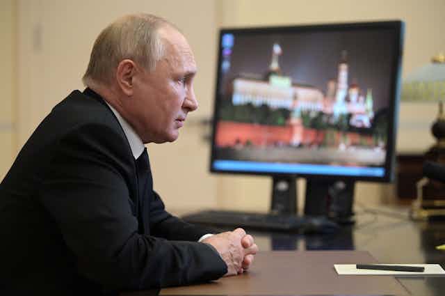 Russian President Vladimir Putin sits at a desk as news of the Russian parliamentary elections plays on a TV.