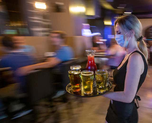 A waitress wearing a mask carries a tray of drinks.
