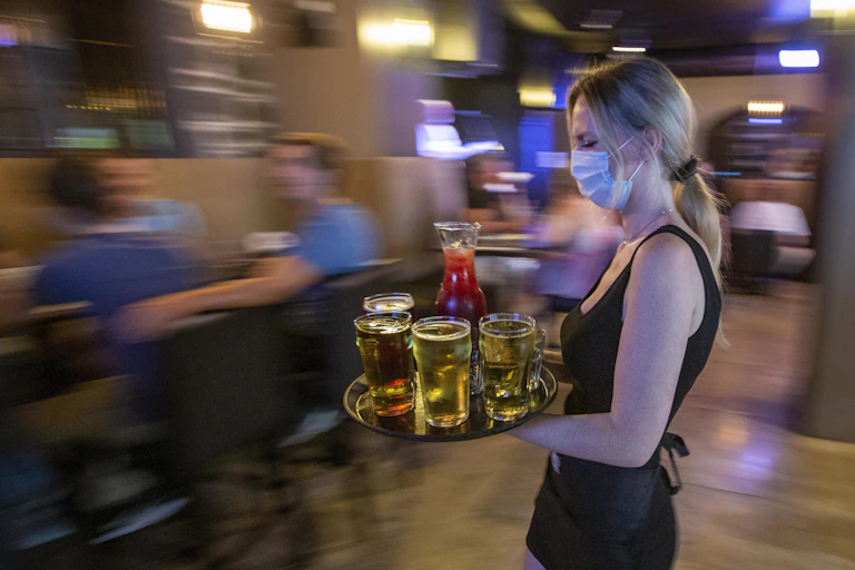 A waitress wearing a mask carries a tray of drinks.
