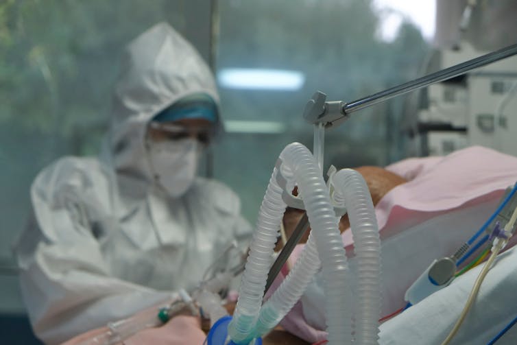 A clinician in full PPE treats a patient with breathing tubes.