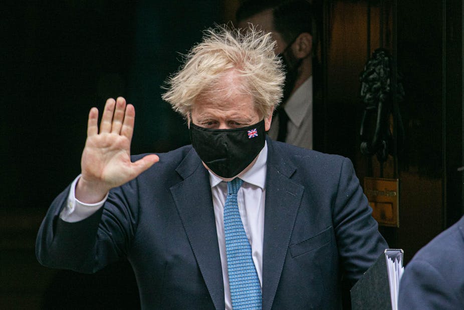 Boris Johnson in facemask holds up hand 