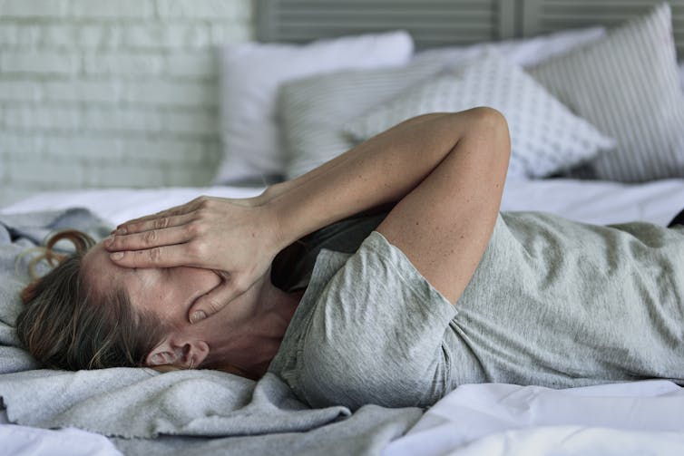 A Woman With Covid Is Lying In Bed, Covering Her Face