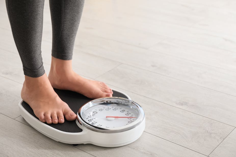 A person stands on a weight scale in bare feet.