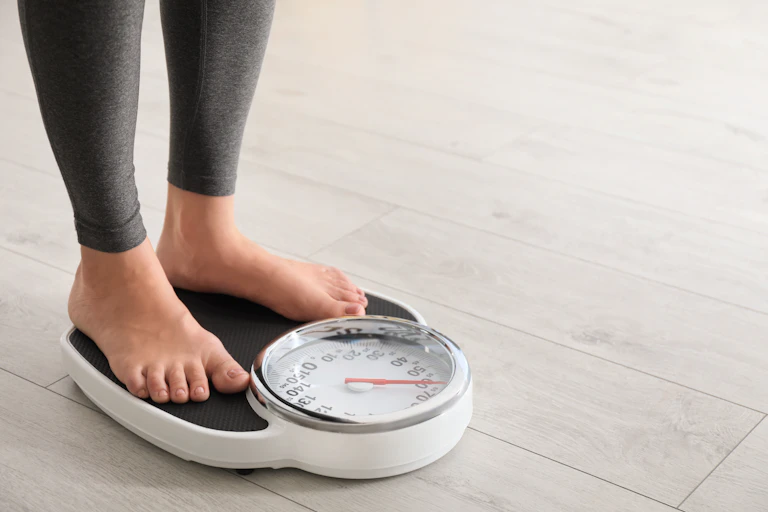 A person stands on a weight scale in bare feet.