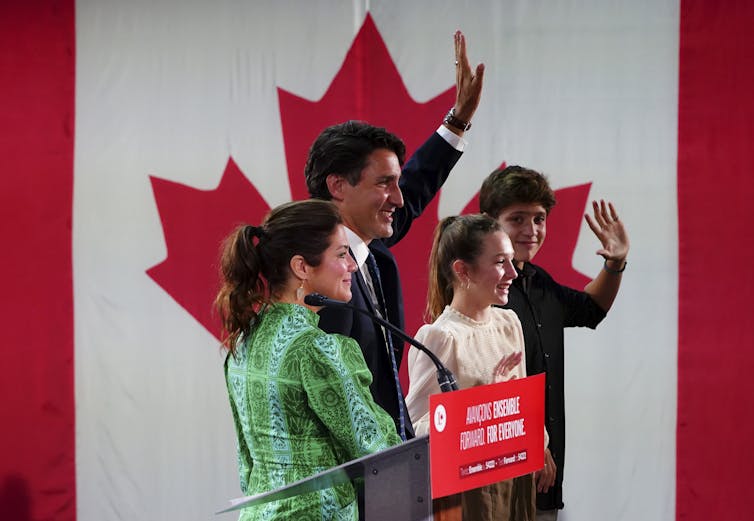 Trudeau and his family wave to supporters with a Canadian flag beside them.