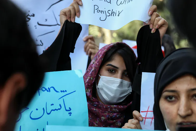 Afghani women, many wearing COVID masks and carrying protest banners in Arabic.