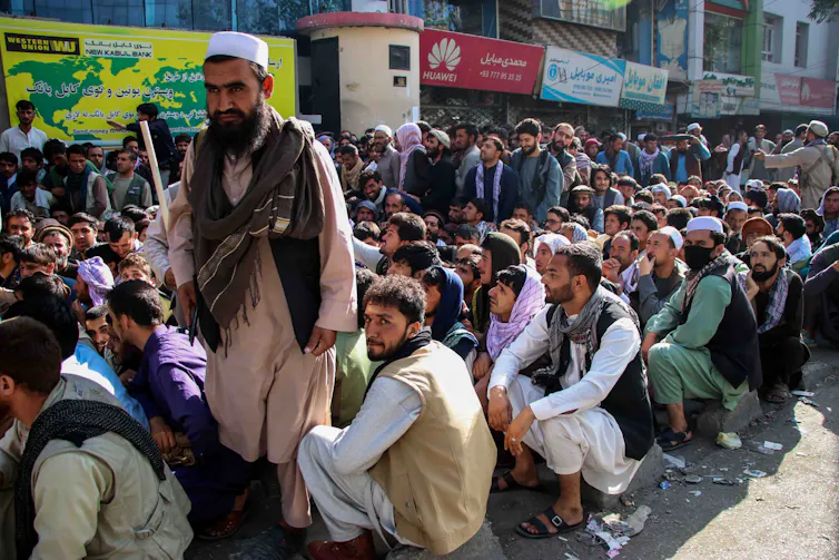 Hundreds of Afghans sit in the street.