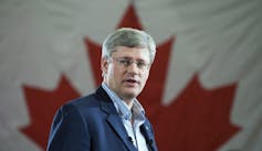 Harper speaks with a Canadian flag behind him.