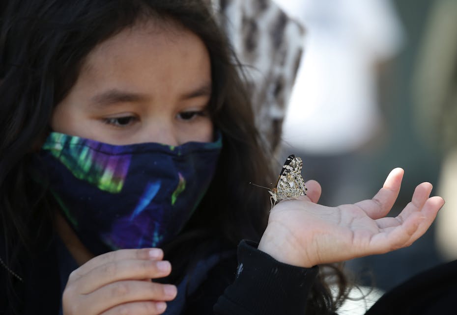 A little girl wears a northern lights mask and holds a butterfly on her hand