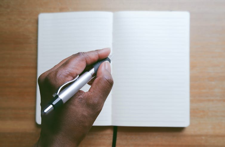 hand with pen poised above empty notebook pages