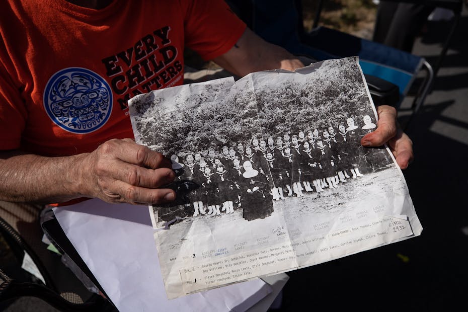 Hands hold an archive photo of St. Paul IRS, it is a 'class-type' photo with nuns flanking the students as well as one perched in the centre