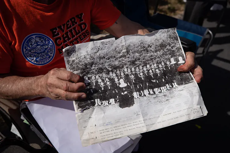 Hands hold an archive photo of St. Paul IRS, it is a 'class-type' photo with nuns flanking the students as well as one perched in the centre