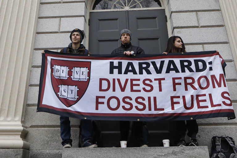 Protesters hold up a banner telling Harvard to divest from fossil fuels.